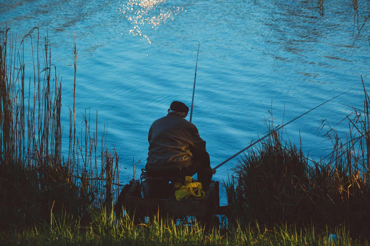 Man Sitting on the Chair While Doing Fishing Near Body of Water